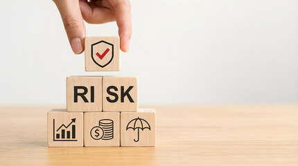 A human hand places a security shield block on wooden cubes spelling RISK with financial growth and protection symbols on a light table