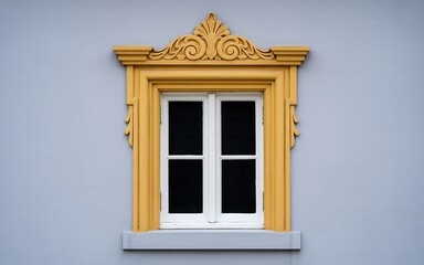 Fototapeta premium Ornate yellow decorative window frame against a pale blue building wall, showcasing traditional architectural detail and craftsmanship.