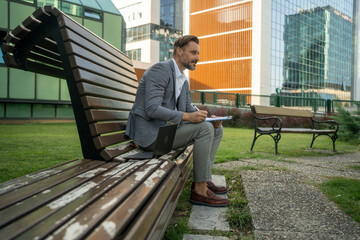 Businessman writing new ideas on bench outdoors, inspired and creative