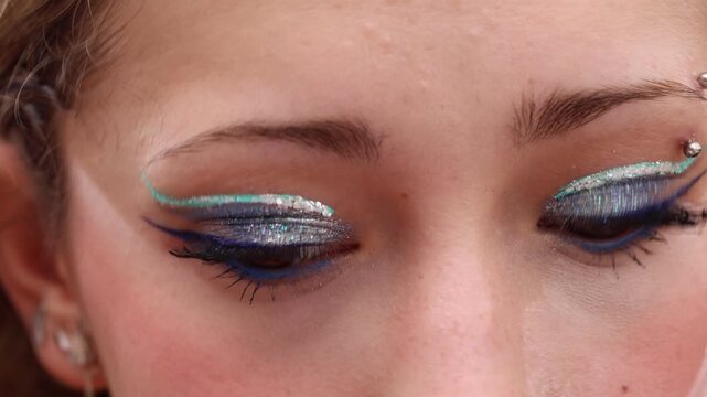 Young woman with creative glitter makeup applying highlighter on her cheekbones with a brush