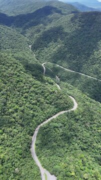 Imagem a&eacute;rea de estrada cortando &aacute;rea montanhosa coberta por vegeta&ccedil;&atilde;o nativa, formando trajeto sinuoso em dire&ccedil;&atilde;o ao litoral de Bertioga.