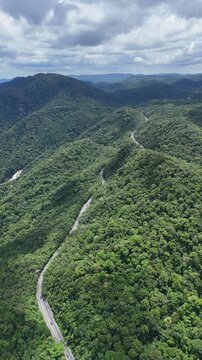 V&iacute;deo drone 4k a&eacute;rea de estrada atravessando montanhas cobertas por floresta nativa, representando o acesso rodovi&aacute;rio ao litoral paulista.