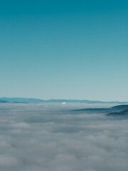 Obraz premium Endless cloud layer covering valleys and hills with distant mountains on the horizon. Soft light creates a dreamy and minimal natural background.