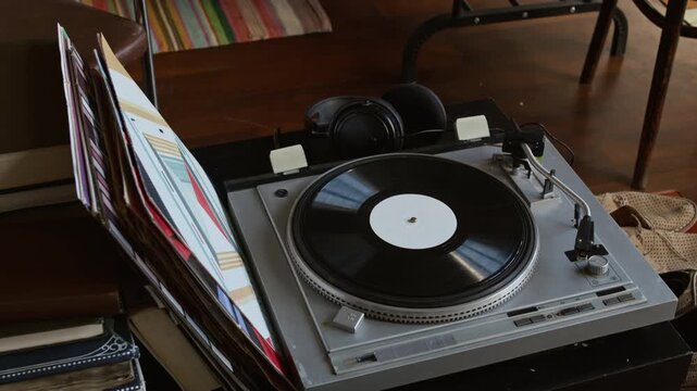 Close-up of vintage music record player, headphones, vinyl discs, stack of old and antique books, displayed on table on sales floor in charity store, trendy retro shopping vibe