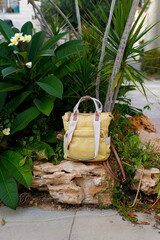 A vibrant yellow backpack placed on a stone ledge surrounded by lush tropical plants and flowers.
