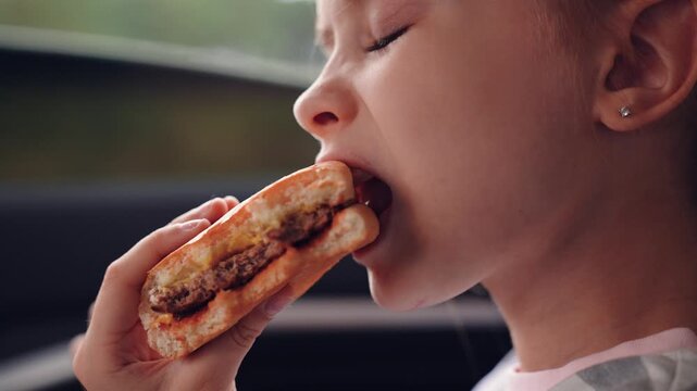 little girl child eating burger in car, happy person, Happy child with delicious burger, Tasty meal hungry traveler, Young girl eating sandwich car seat, Road trip lunch break children, Eating fast