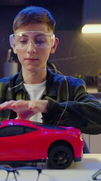 Teenage boy vlogger is recording video using smart phone about assembling and testing electric circuit building and programming car in evening at home. Slow motion.