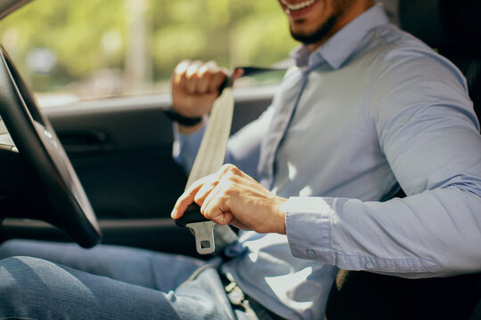 Cropped of arab guy in formal outfit fastening automobile seatbelt, closeup of middle-eastern man entrepreneur driving nice car, going to office, sde view, copy space. Safety driving concept