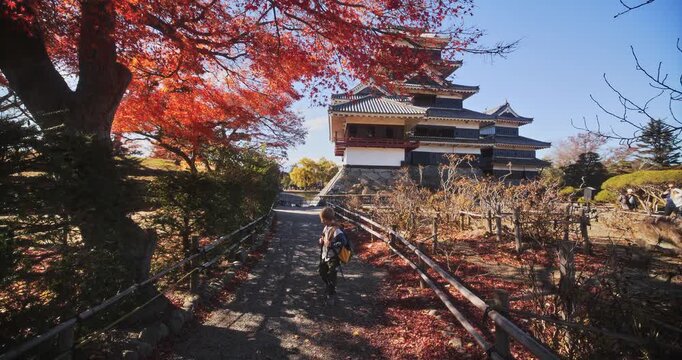 Kid with backpack walking alone on autumn trail away from legendary 16th century castle - slow motion