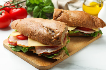 Obraz premium Delicious baguette sandwiches with ham, cheese and vegetables on white marble table, closeup