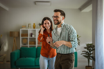 Fototapeta premium Happy couple laughing singing karaoke enjoying fun leisure time at home