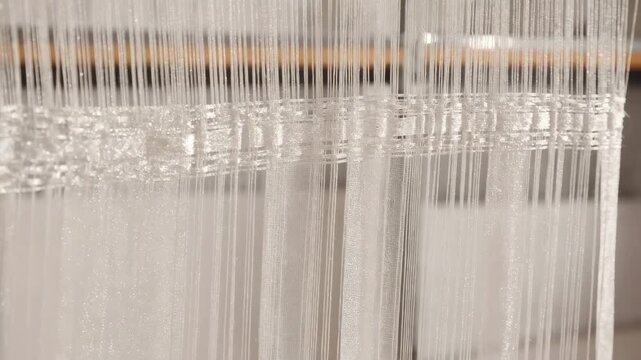 Medium shot of intricate organzastyle fabric production highlighting shimmering translucent threads interlaced to form a crisp elegant curtain material with subtle stiffness.
