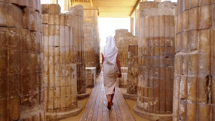 A woman walking through ancient stone columns in Egypt, enjoying a peaceful vacation and cultural travel experience.