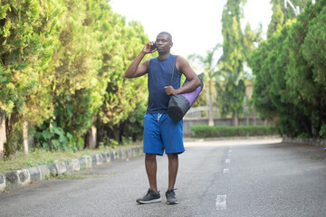 Obraz premium Young Man On Phone In Quiet Street With Gym Bag, Casual Fitness Traveler