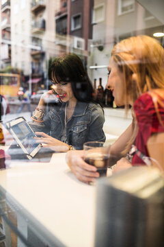 Young people in their twenties look at a tablet inside a bar while having drinks.
