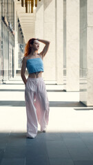 A portrait of a teenage girl with red hair posing for a photo near columns at the entrance to a business center