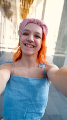 A teenage girl poses and smiles for a selfie on a smartphone.