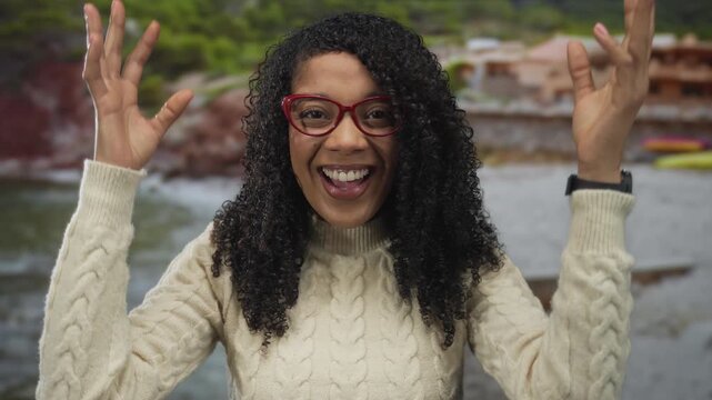 African american woman with open mouth and hands to head at building near seaside beach in daylight; surprise.