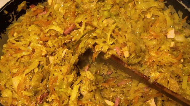 Preparing of traditional dish bigos with sausage, meat, carrot and cabbage on a frying pan, stewed cabbage. 