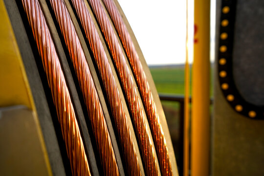 Industrial yellow tensioning machine laying thick bare copper wire for electrical infrastructure development outdoors.
