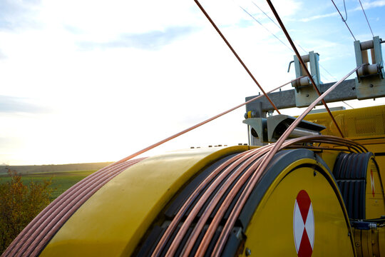 Industrial yellow tensioning machine laying thick bare copper wire for electrical infrastructure development outdoors.