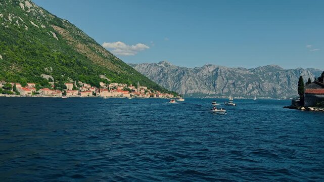 Montenegro, picturesque scenery of seaside promenade on a sunny day, moored boats, brick-colored tiled roofs, a mountain range in the background