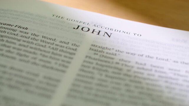 Bible John book pages turn during a close up study of holy scripture. A detailed shot of flipping white paper in the New Testament Gospel book focusing on the divinity and word of Jesus.