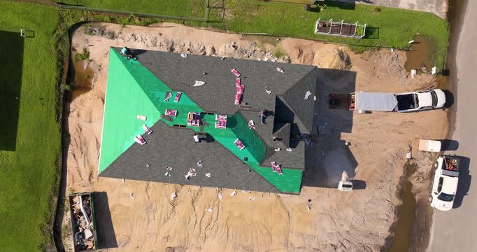 Construction workers installing asphalt shingles on residential home. New house rooftop being built.