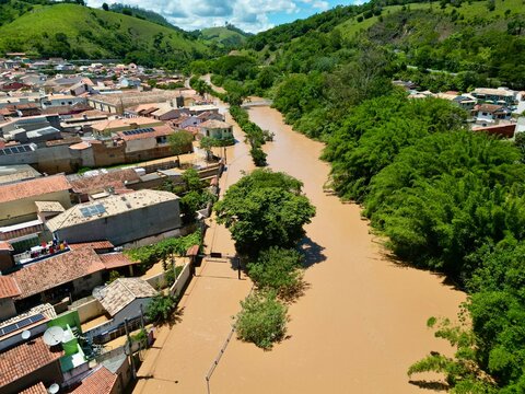 Vista a&eacute;rea por drone de uma enchente urbana, mostrando ruas alagadas, casas parcialmente submersas e o impacto das chuvas intensas. Conceito de desastre natural, mudan&ccedil;as clim&aacute;ticas, crise ambiental.