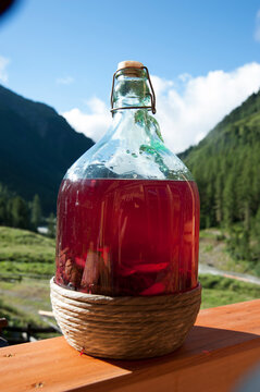 Tyrolean Swiss stone pine liqueur (Zirbala) infusing in glass demijohn bottle on sunny alpine balcony, mountain valley background
