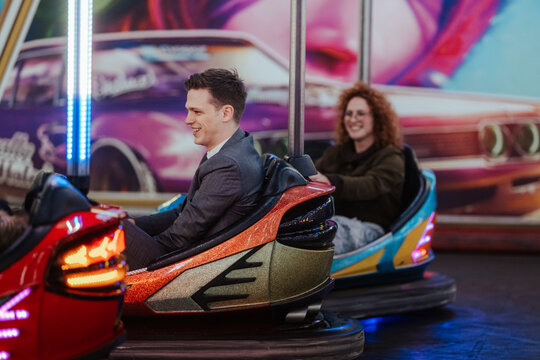Young man and woman riding bumper cars at amusement park