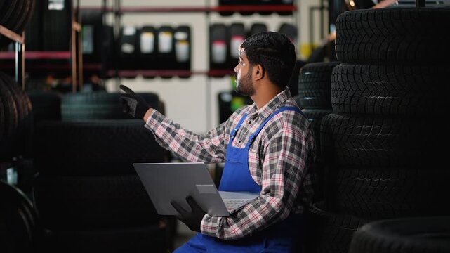 Mechanic checking tire inventory using laptop in a garage warehouse