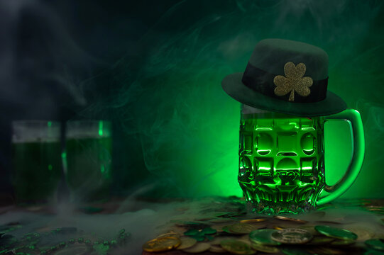 Green beer, hat and clover leaves on grey wooden table. St. Patrick Day celebration