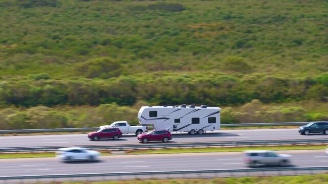 Travelling with camper during road trip in USA. Truck towing RV trailer driving down American freeway at high speed. Travel transportation infrastructure.