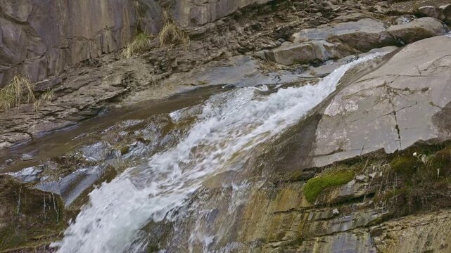 View of a detail of a small waterfall among rocks in the mountains. Water flowing with splashes through wet rocks and stones