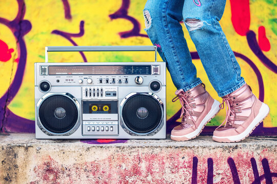 girl in streetwear jeans and boots carrying a retro boombox against graffiti wall, urban energy