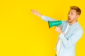 Young man holding a megaphone and pointing to the side while shouting on a vibrant yellow background
