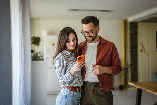 Smiling couple enjoying digital content on smart phone at home