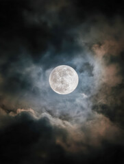 Bright full moon shining through dramatic clouds in a dark night sky creating a mysterious and captivating celestial scene with contrasting shadows and light