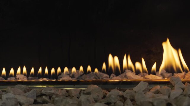 Detailed close-up of a row of vibrant yellow flames emerging from a gas burner tube, surrounded by white decorative pebbles in a modern