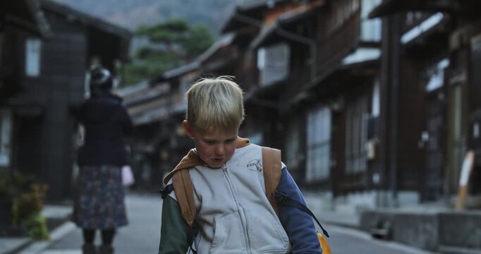 Silly boy doing little dance while standing on street of old Japanese village - medium shot