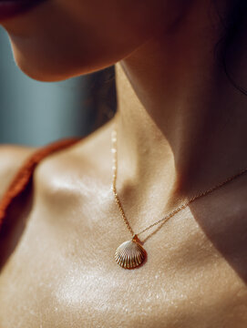 Woman wearing delicate gold shell pendant necklace highlighting glowing skin on her neck and collarbone in soft natural light