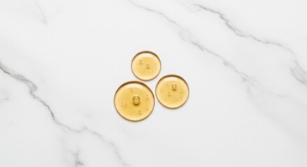 A cluster of three viscous golden serum drops resting on a white marble surface with grey veins.