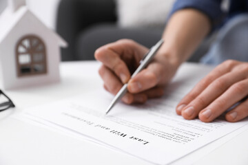Woman signing Last Will and Testament at white table indoors, closeup