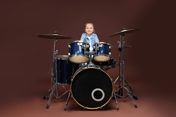 Little girl learning how to play drums on brown background