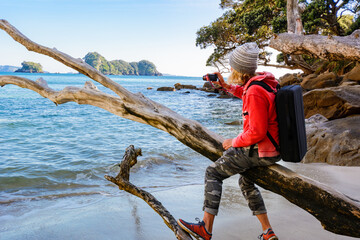 Woman Sitting on Driftwood at Beach Looking at Ocean in New Zealand