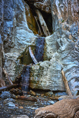 Waterfall Cascading Over Limestone Rocks and Driftwood in Rugged Mountain Canyon