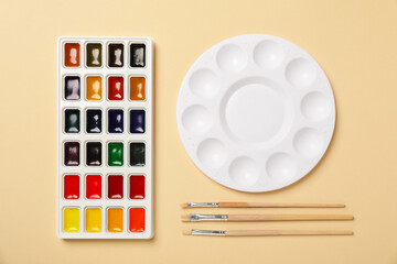 Obraz premium Watercolor paints, palette and brushes on beige background, flat lay