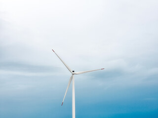 Fototapeta premium Single wind turbine against soft cloudy sky. Minimal renewable energy concept with copy space. Clean electricity production, sustainable technology and environmental power generation.