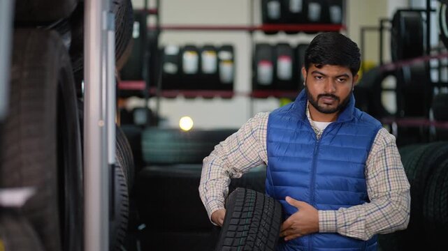 Indian mechanic taking new car tire from shelf in auto repair shop